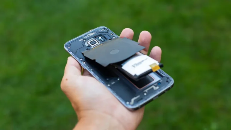 Close de uma bateria de celular estufada sendo examinada por um técnico em uma bancada de assistência técnica.